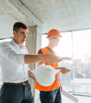Planning the process. Man in suit and handyman in orange protective wear is working on construction